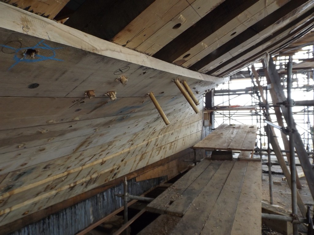 The trunnels on the left have been pounded in and need to be trimmed flush withthe plank.  Those on the right need to be finished.