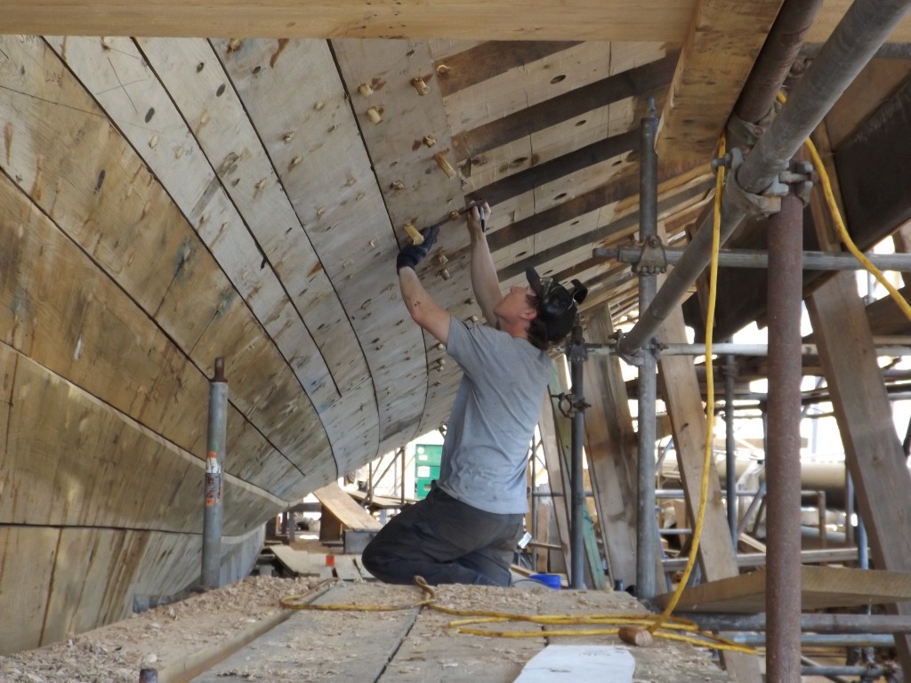 Willy is measuring where the fastenings are in the frame and making notations on the plank below.  When the next plank is clamped in position the crew can refer to the notes when they drill teh holes for the fastenings.