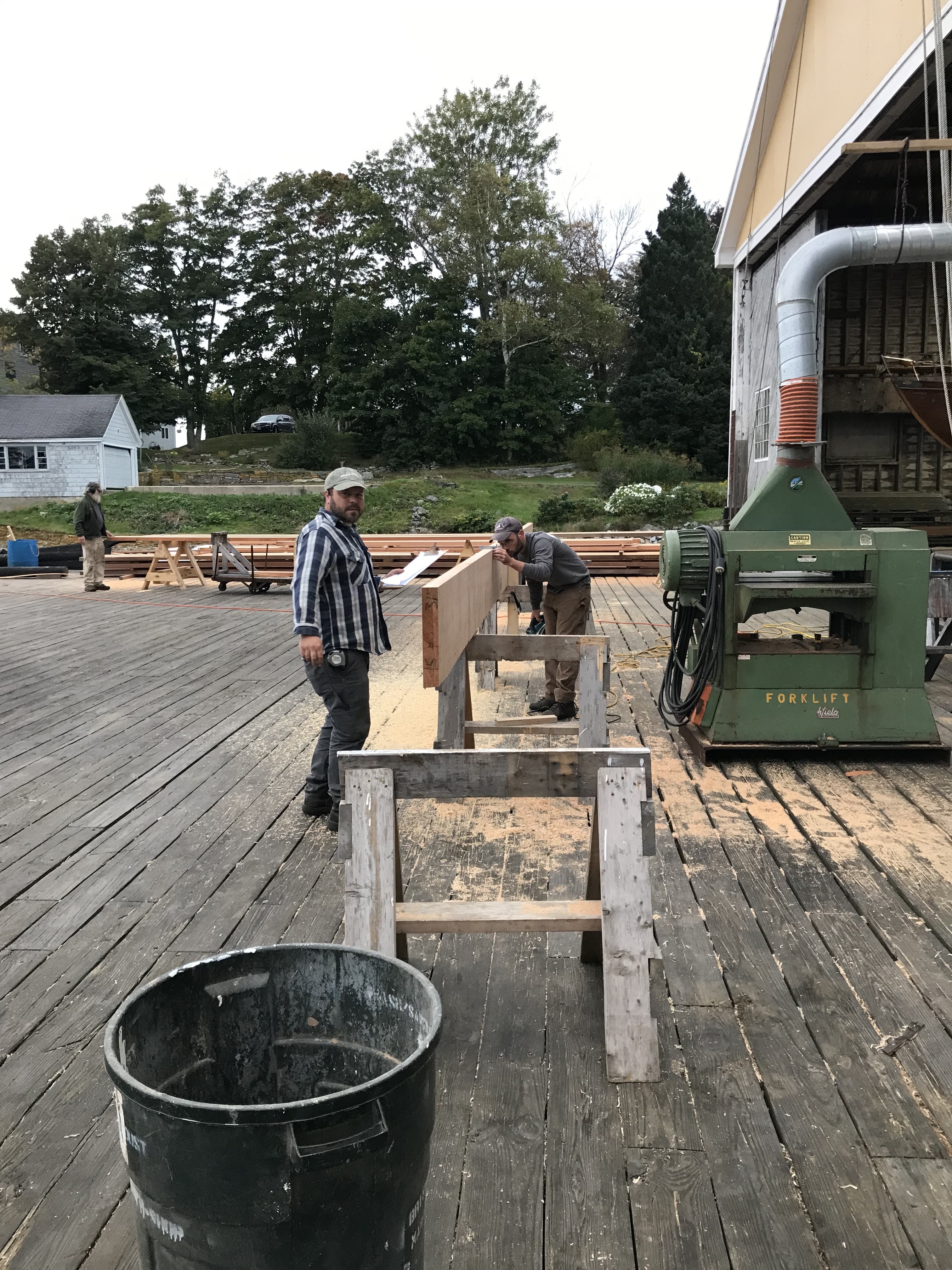 Preparing material Jason and Sam Perkins are working together using the planer to bring raw lumber into specific thicknesses and widths necessary for the lamination process. Each board is numbered and is marked to fit into a particular spar in a particular spot. This lamination plan requires absolute accuracy in the preparation of each piece of lumber to ensure that the finished product meets required dimensions.